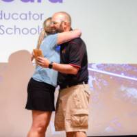 Teacher receives hug from Groundswell staff in front of projected "school educator" background